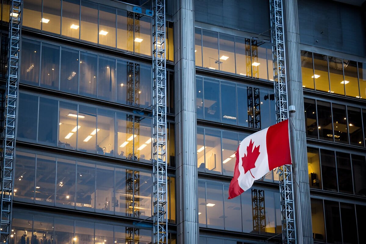 Canadian flag waving in front of a modern office building with glass windows